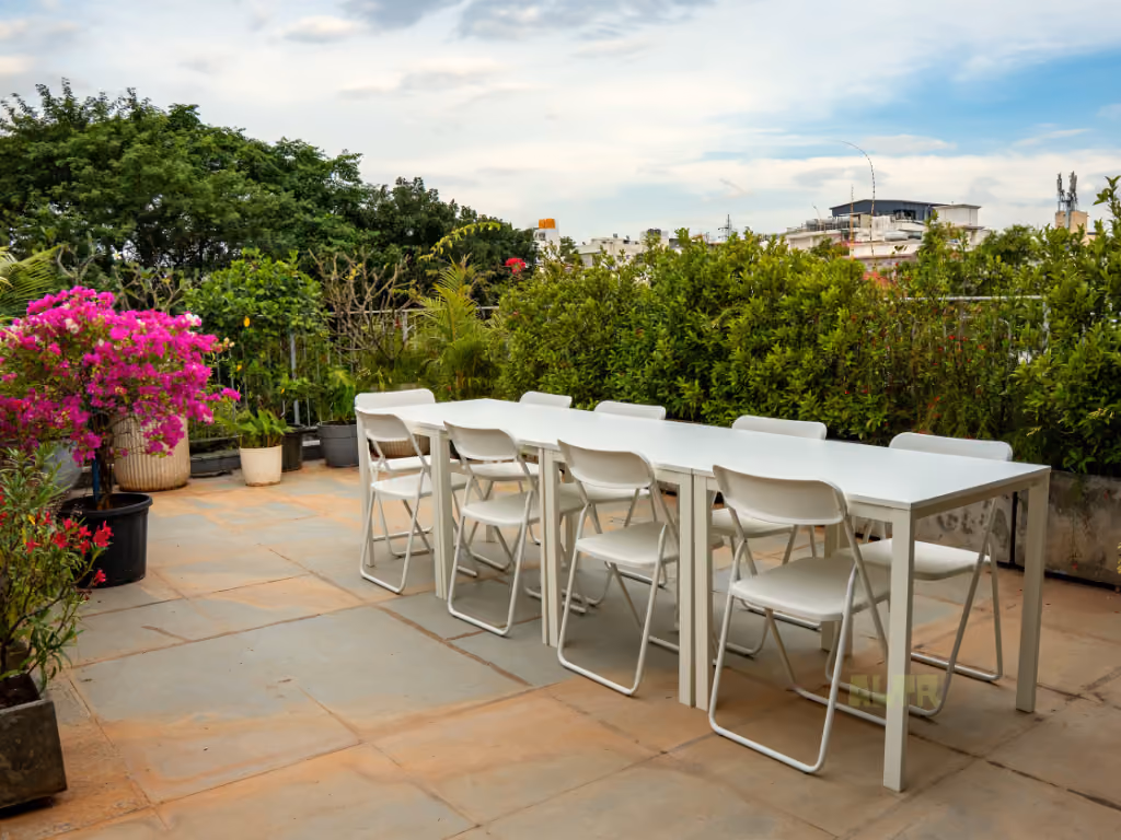A long white table and chairs on the roof terrace, bougainvillea in flower beside it